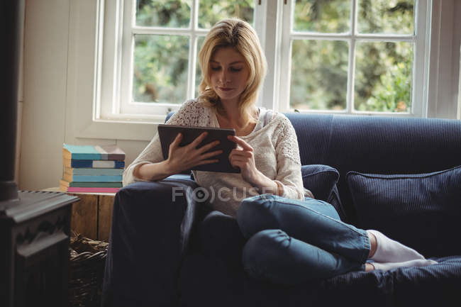 Mulher bonita sentada no sofá com mesa digital na sala de estar em casa — Fotografia de Stock