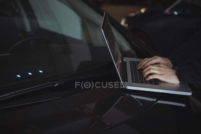 Hands of man using laptop on car in garage — Stock Photo