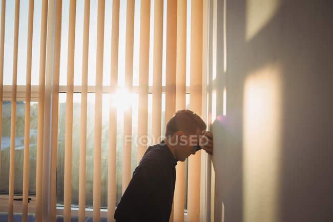 Hombre trastornado apoyado en la pared en la oficina - foto de stock