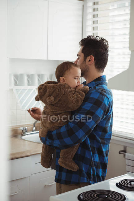 Отец держит ребенка, стоя дома на кухне — стоковое фото
