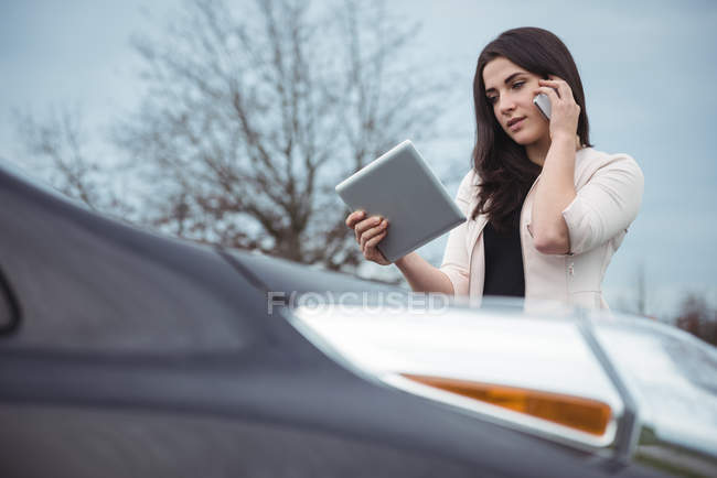 Красива жінка розмовляє на мобільному телефоні, використовуючи цифровий планшет на вулиці — стокове фото