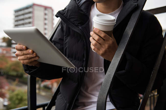 A meio da seção do homem usando tablet digital enquanto toma café na varanda — Fotografia de Stock
