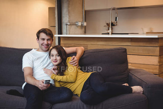 Улыбающаяся пара сидит на диване и смотрит телевизор в гостиной дома — стоковое фото