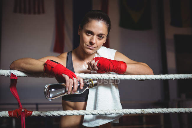 Portrait of female boxer holding water bottle in boxing ring — Stock Photo