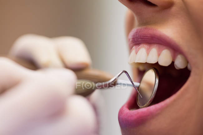Close-up de dentista examinando paciente do sexo feminino com ferramentas na clínica odontológica — Fotografia de Stock