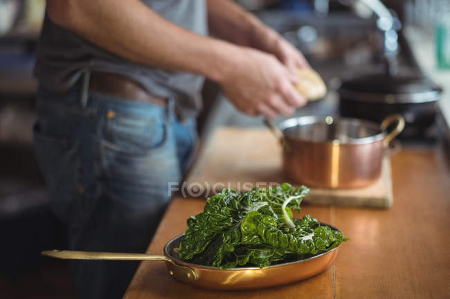 Lechuga fresca lavada en sartén y hombre preparando comida en la cocina - foto de stock