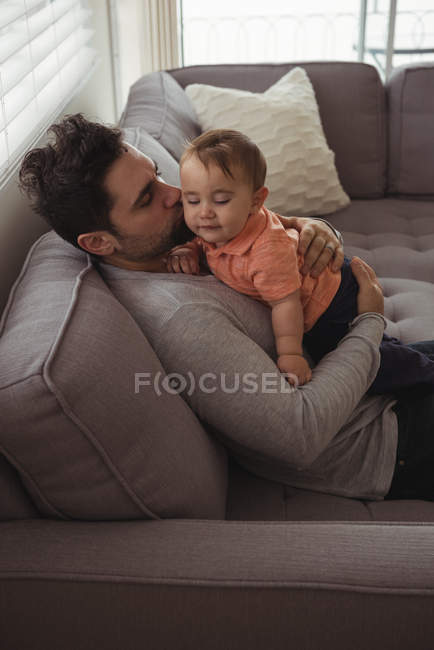 Отец целует своего ребенка на диване в гостиной дома — стоковое фото