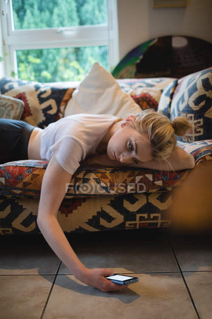 Mujer acostada y el uso de teléfono móvil en el sofá en la sala de estar en casa - foto de stock