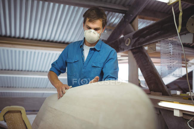 Mann mit Maske bastelt Surfbrett in Werkstatt — Stockfoto