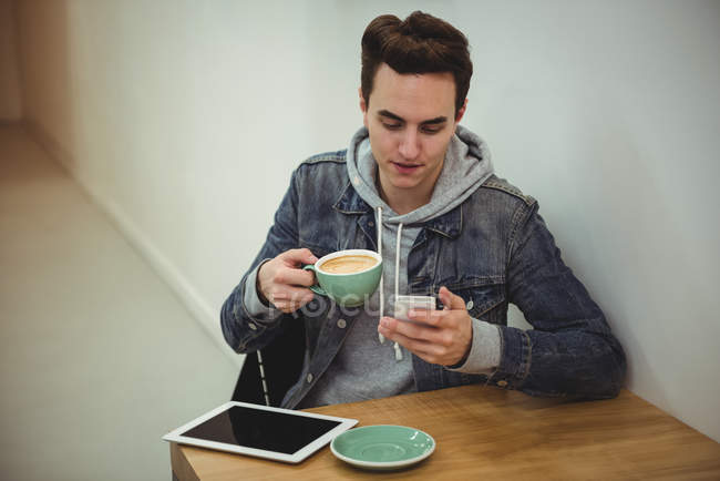 Homem usando telefone celular enquanto segurando xícara de café na cafeteria — Fotografia de Stock