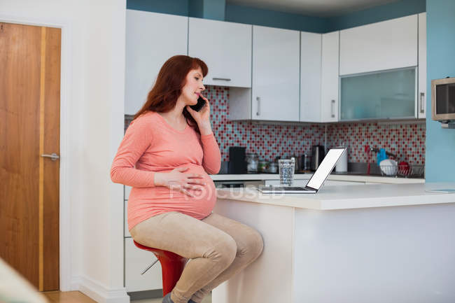 Donna incinta che parla al telefono cellulare in cucina a casa — Foto stock