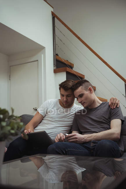 Гей пара сидить на дивані і дивиться на цифровий планшет вдома — стокове фото
