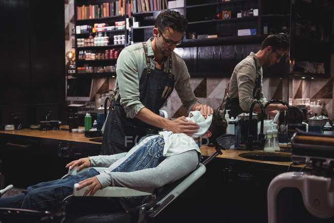 Barber applying hot towel on client face in barber shop — Stock Photo