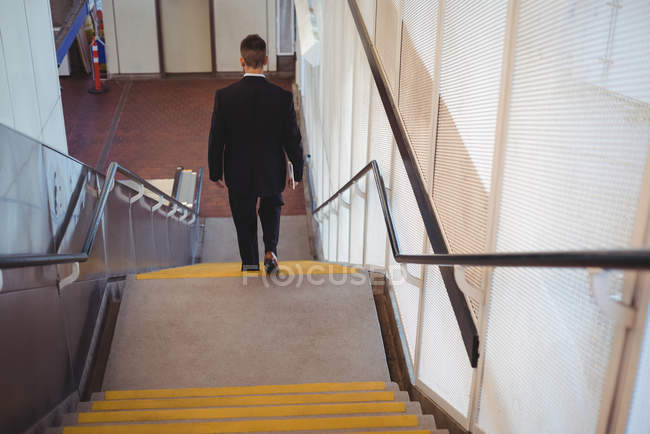 Вид ззаду бізнесмена з щоденником, що йде по сходах в офісі — стокове фото