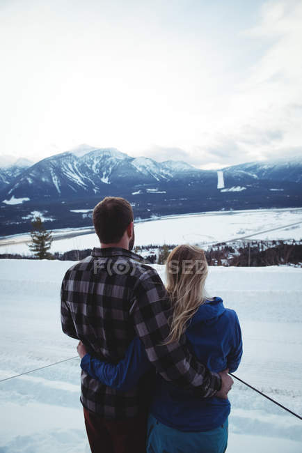 Couple with arms around standing on snow covered field against sky — Stock Photo