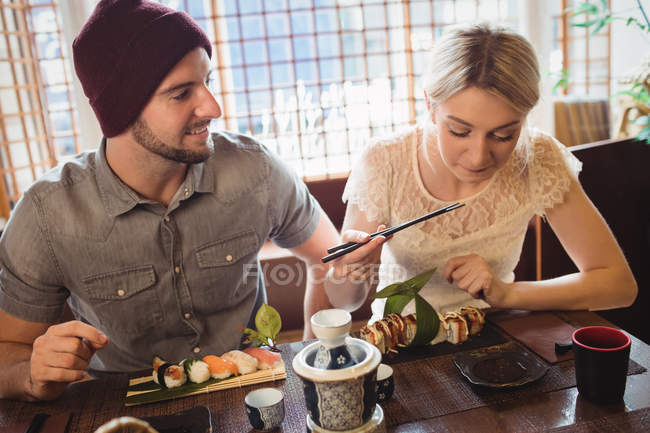 Пара взаимодействует друг с другом во время еды суши в ресторане — стоковое фото