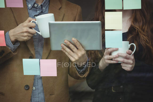 Ejecutivos de negocios discuten sobre tabletas digitales mientras toman una taza de café en la oficina - foto de stock