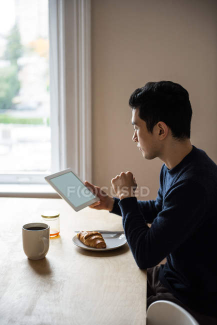 Man using digital tablet while having breakfast at home — Stock Photo