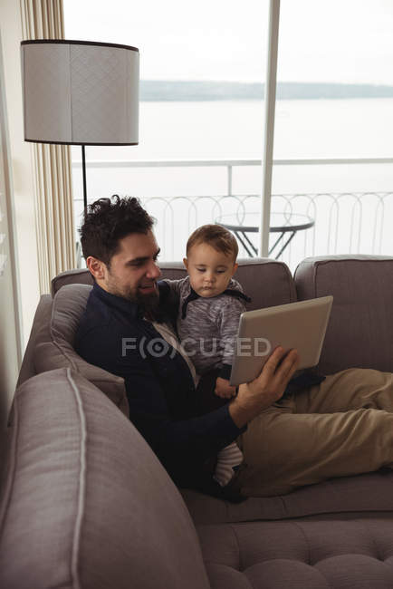 Father using digital tablet while holding his baby at home — Stock Photo
