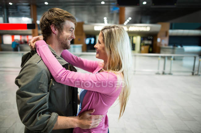 Pareja alegre abrazándose en la sala de espera en la terminal del aeropuerto - foto de stock