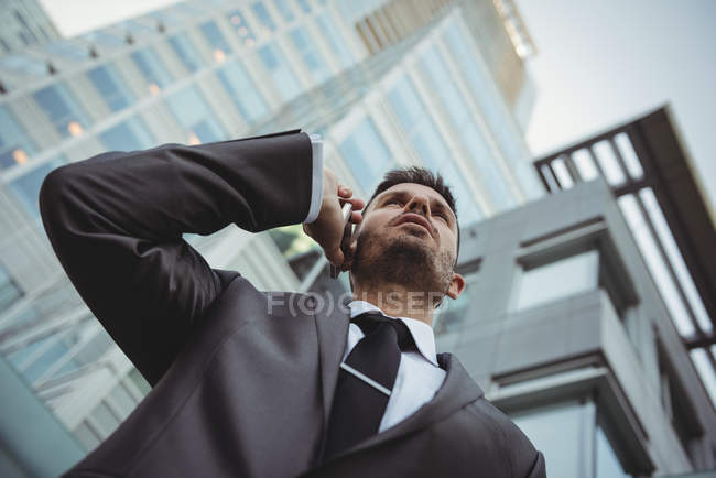 Vue en angle bas de l'homme d'affaires parlant sur le téléphone portable près de l'immeuble de bureaux — Photo de stock