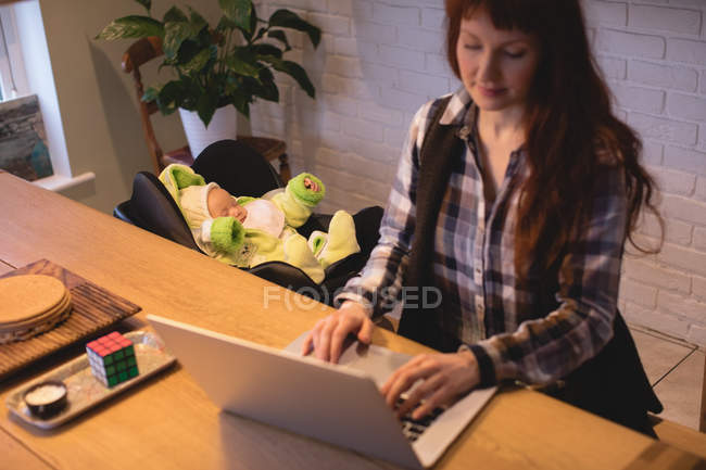 Mother using laptop while care of baby at home — Stock Photo
