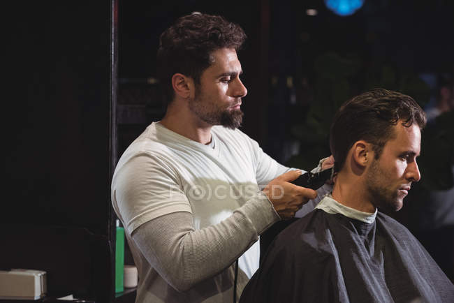 Hombre consiguiendo pelo recortado por peluquero con trimmer en peluquería - foto de stock