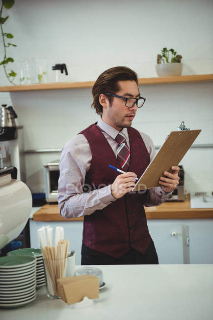 Man writing with pen on clipboard in coffee shop — Stock Photo