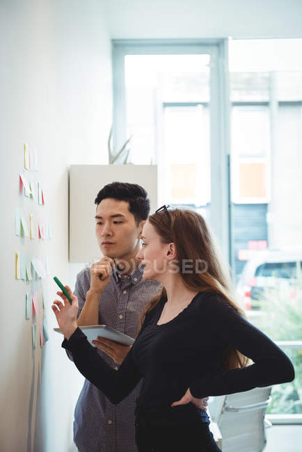Ejecutivos de negocios discutiendo sobre notas adhesivas en la oficina - foto de stock