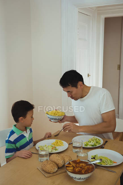 Vater serviert seinem Sohn zu Hause Essen am Esstisch — Stockfoto