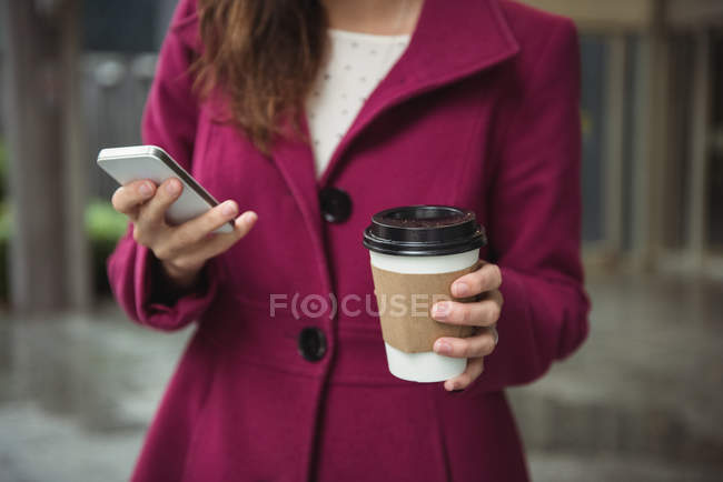 Mid section of businesswoman holding disposable coffee cup and using mobile phone — Stock Photo