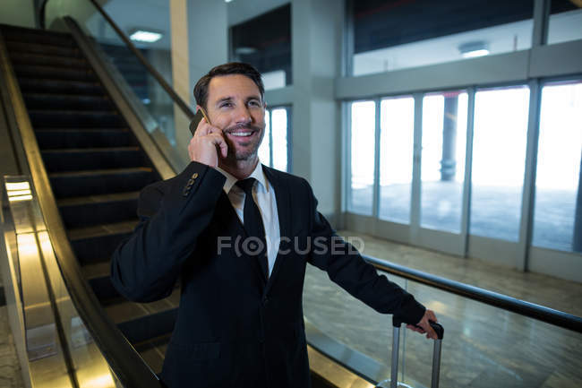 Empresario en escalera mecánica hablando por teléfono móvil en el aeropuerto - foto de stock