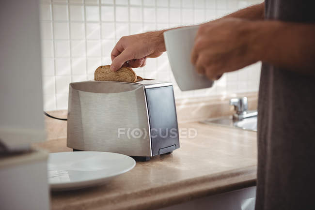 Sección media del hombre pan tostado para el desayuno y beber café en la cocina - foto de stock