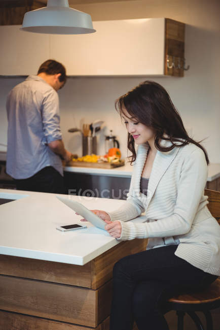 Femme utilisant tablette numérique tandis que l'homme travaillant en arrière-plan à la cuisine — Photo de stock