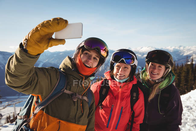 Три улыбающиеся лыжницы зимой делают селфи на мобильном телефоне — стоковое фото