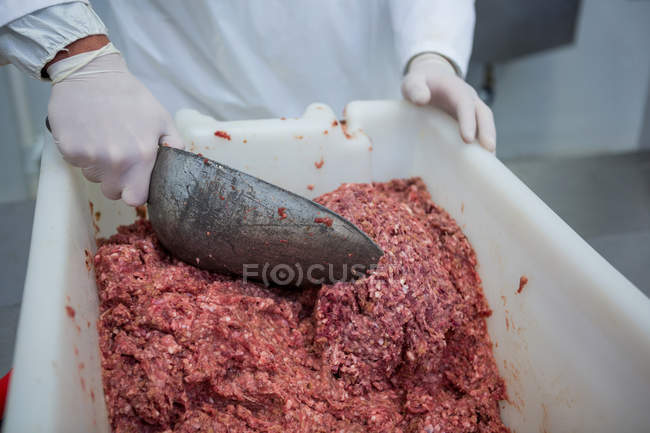 Mid section of butcher using scoop for removing minced meat from container at meat factory — Stock Photo