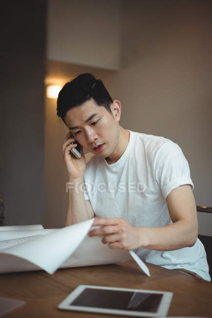 Geschäftsführender Angestellter telefoniert mit dem Handy, während er sich im Büro den Bauplan ansieht — Stockfoto