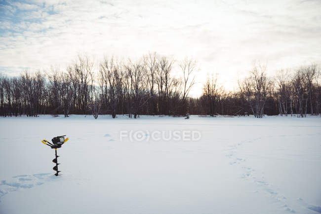 Taladro de pesca en hielo en el paisaje nevado y árboles - foto de stock