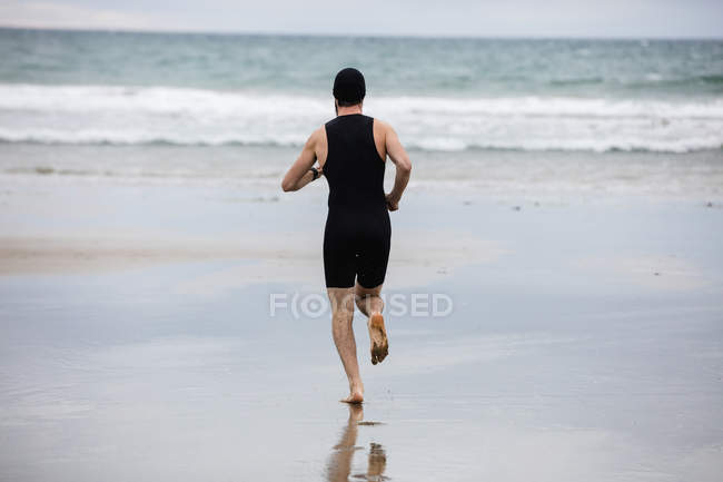 Visão traseira do homem em traje de natação e touca de natação correndo na praia — Fotografia de Stock