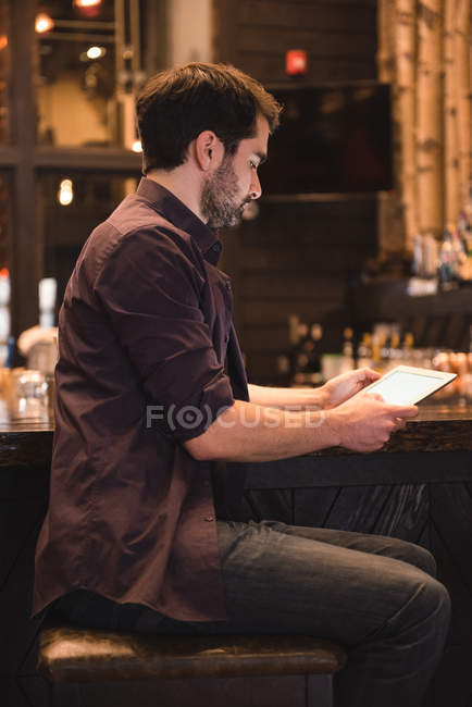 Schöner Mann sitzt an der Theke und nutzt digitales Tablet — Stockfoto