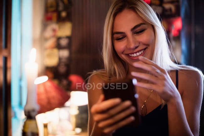 Mulher sorridente bonita usando telefone celular no bar — Fotografia de Stock