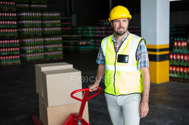 Jovem trabalhador do sexo masculino puxando carrinho no armazém — Fotografia de Stock