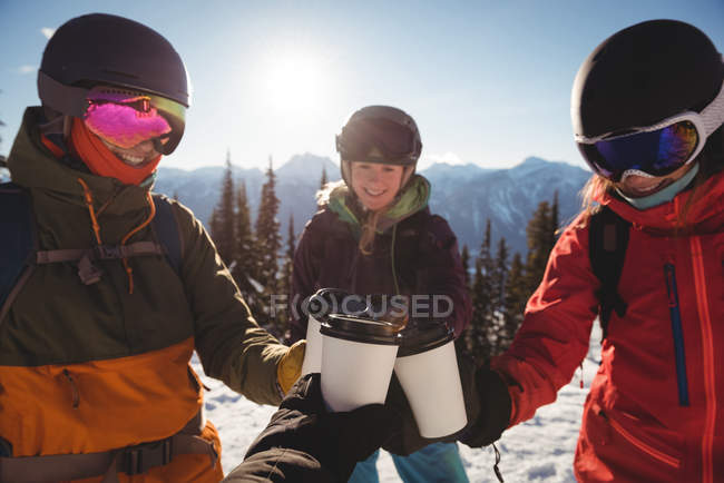 Esquiadores sonrientes brindan por tazas de café en montañas cubiertas de nieve - foto de stock