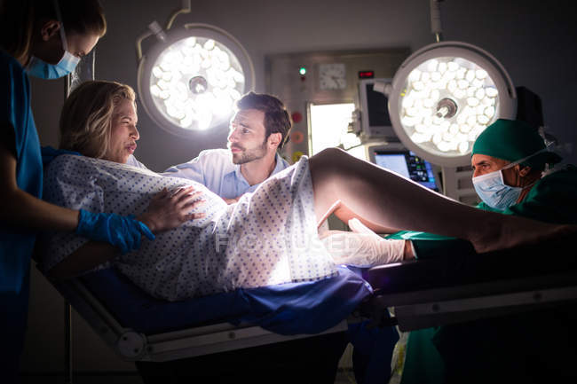 Доктор вивчає вагітну жінку під час пологів, а чоловік тримає руку в операційній кімнаті — стокове фото