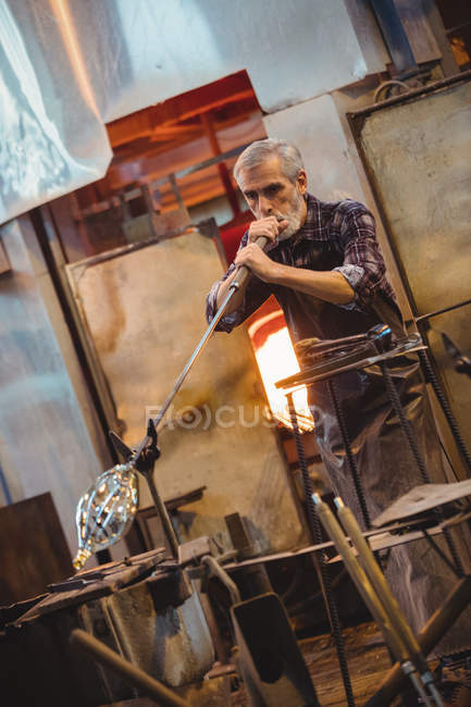 Soffiatore di vetro che modella un vetro sul blowpipe alla fabbrica di soffiaggio del vetro — Foto stock