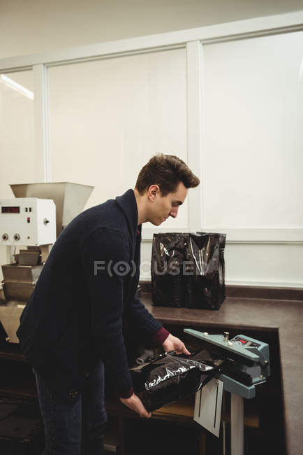 Man packing coffee bag from sealing machine in coffee shop — Stock Photo