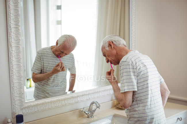 Homem sênior escovando os dentes no banheiro — Fotografia de Stock