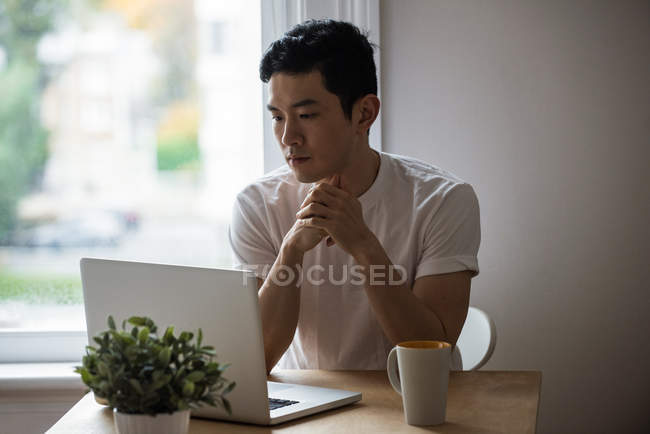 Человек смотрит на ноутбук с чашкой кофе на столе дома — стоковое фото