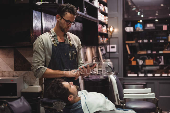 Barbeiro procurando estilo barba em tablet digital na barbearia — Fotografia de Stock