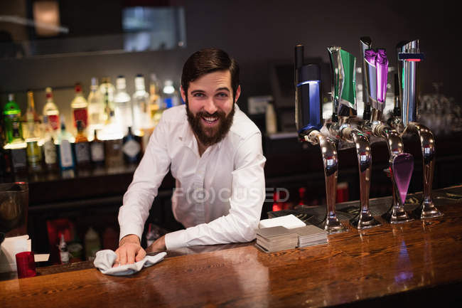 Портрет улыбающегося бармена, убирающего барную стойку в баре — стоковое фото